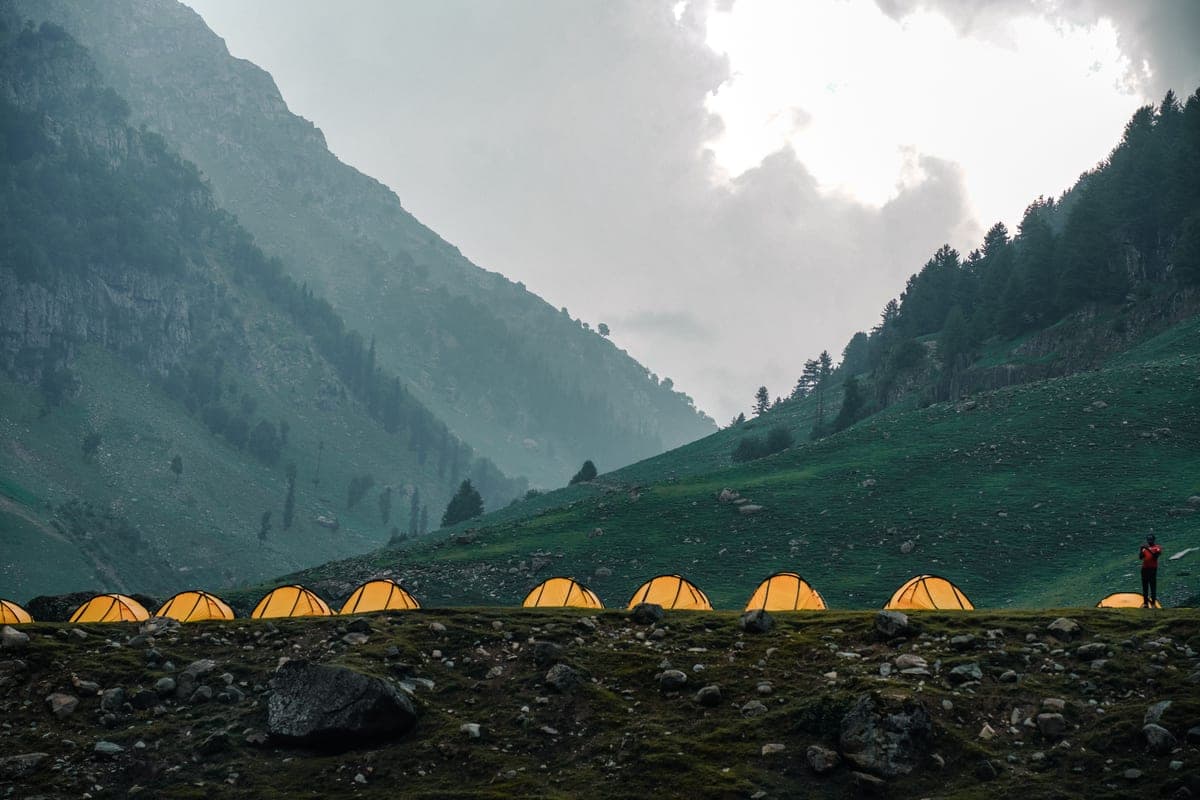 A mountain campsite with lit tents under a cloudy evening sky