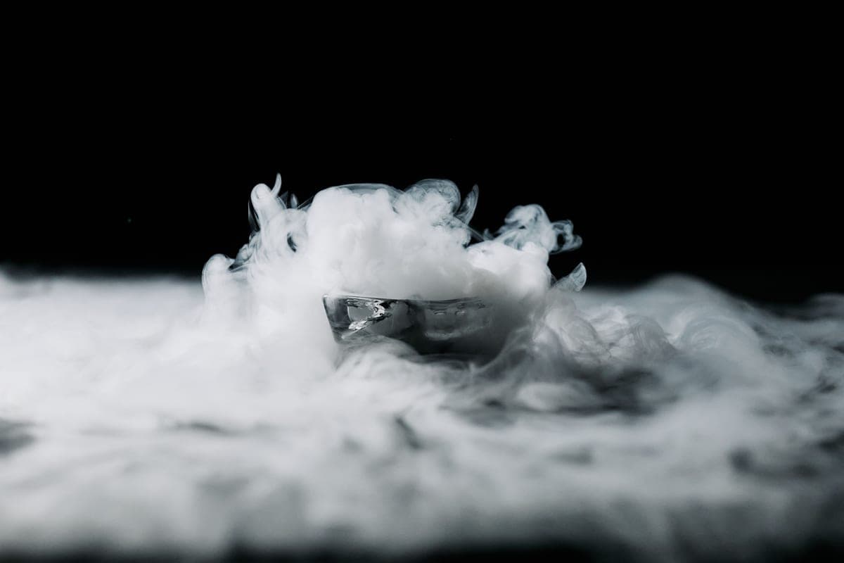 White vapor drifting over an ice cube against a black background