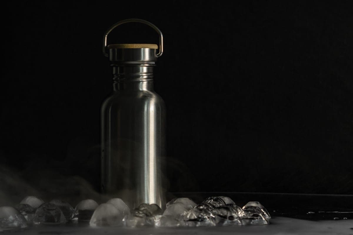 Illustrative stock photo: a stainless steel flask surrounded by ice cubes on a dark surface