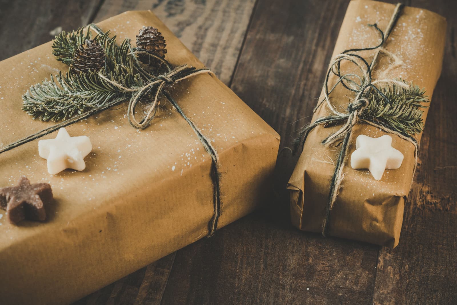 Two presents wrapped in brown kraft paper with pine sprigs on a wooden table
